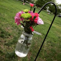 a vase filled with flowers sitting on top of a grass covered field next to a metal pole