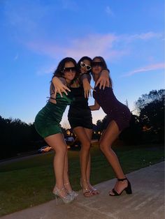 three young women are posing for the camera in front of a blue sky and green grass