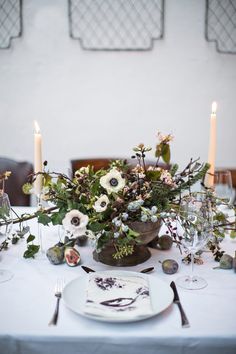 the table is set with white plates and silverware, candles, and flowers in vases