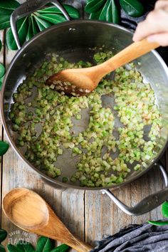 peas being cooked in a pan with wooden spoons and green leaves around it on a wood table