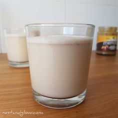 two glasses filled with milk sitting on top of a wooden table next to each other