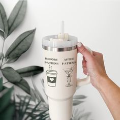 a hand holding a coffee cup next to a plant