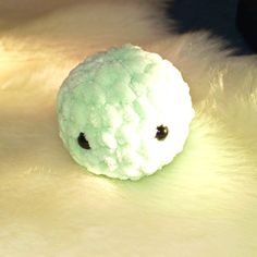 a small white stuffed animal sitting on top of a fur covered surface with black eyes