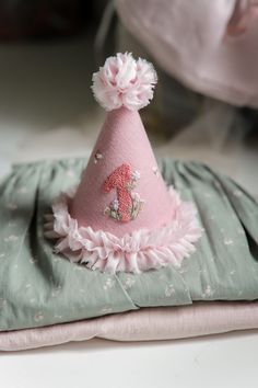 a pink hat with flowers on it sitting on top of a green cloth covered pillow