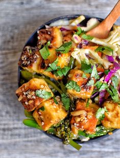 a bowl filled with vegetables and tofu on top of a wooden table next to chopsticks