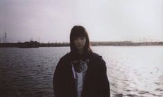 a woman standing in front of a body of water wearing a black jacket and white shirt