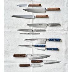 several different types of knives lined up on a white towel with blue handles and wood handles