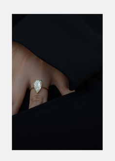 a woman's hand wearing a gold ring with a pear shaped diamond