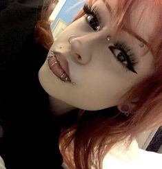 a close up of a person with red hair and piercings on her nose, looking at the camera