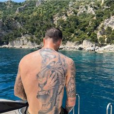 a man with a tiger tattoo on his back sitting in a boat looking out at the water