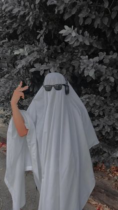 a person dressed as a nun pointing at something in front of some bushes and trees