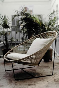 a wicker lounge chair with white pillows on the floor next to potted plants