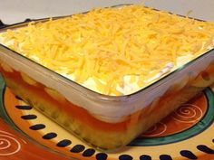 a casserole dish filled with cheese on top of a colorful tablecloth and plate