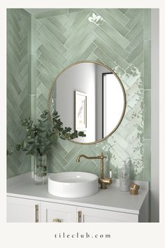 a bathroom with green tiles and a round mirror on the wall above the sink, along with a plant in a vase