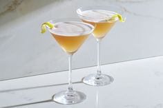 two glasses filled with drinks sitting on top of a white counter next to each other