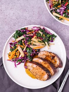 two white plates with meat, vegetables and salad on them next to utensils