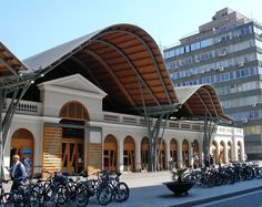 many bicycles are parked in front of a large building with arched windows and wooden roof