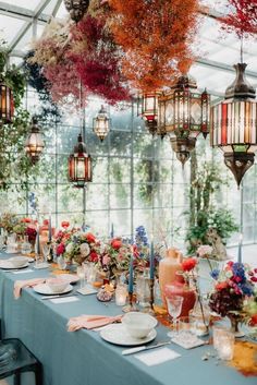 a long table is set with plates and place settings in front of hanging lanterns filled with flowers