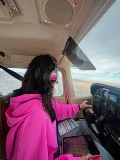 a woman sitting in the cockpit of an airplane with headphones on and looking at her tablet