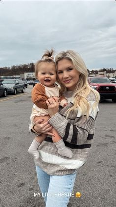 a woman holding a baby in her arms while standing in a parking lot with other cars