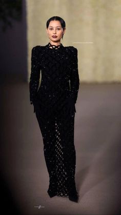 a woman is walking down the runway in a black dress with long sleeves and high slits