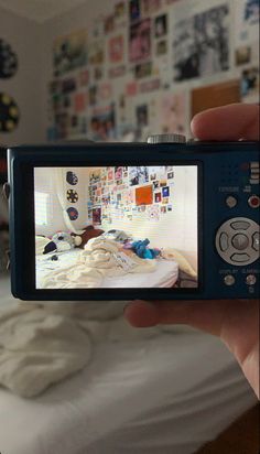 a person holding up a camera to take a photo in front of a bed with pictures on the wall