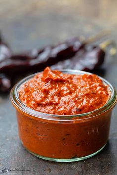 a glass jar filled with red sauce next to some chili peppers