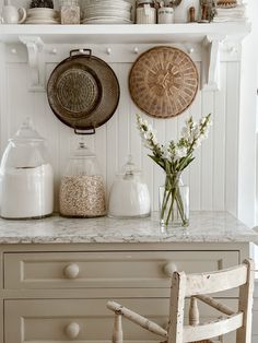 a kitchen counter with plates and vases on top of it next to a wooden chair