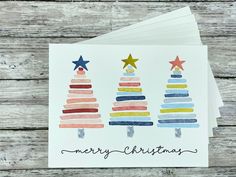 three christmas cards with watercolor trees and stars on them, one has the words merry christmas