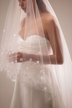 a woman wearing a wedding veil with white flowers on the bottom and side of her veil