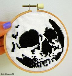 a hand holding a cross - stitched skull in front of a white wall hanging