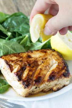 a person is picking up a lemon wedge from a plate with chicken and spinach