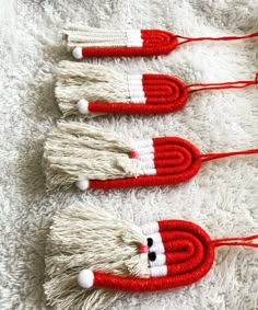 three red and white knitted santa claus ornaments on a white rug with pom - poms