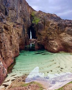 the water is green and clear in this rocky area with a waterfall coming out of it