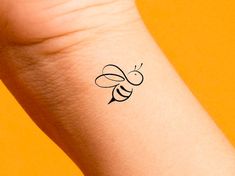 a small tattoo on the wrist of a woman's arm with a bee drawn on it