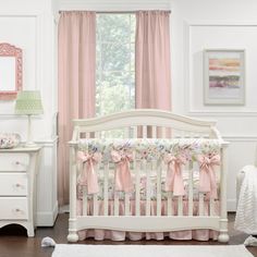 a white crib with pink bows on it in a room next to a window