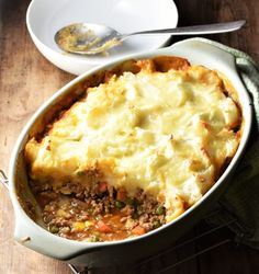 a casserole dish with meat and vegetables in it on a wooden table next to a white plate