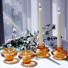 three candles sitting on top of a table next to some glass bowls with flowers in them