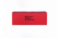 a red spiral notebook with the words brilliant weekly scheduler written in black on it