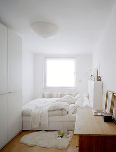 a white bedroom with a bed, desk and dresser in it's corner area