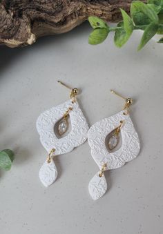 two pairs of white and gold earrings on top of a table next to a plant