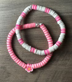 two pink and white bracelets with flowers on them sitting on top of a wooden table