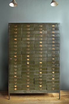 an old metal filing cabinet with lots of drawers on it and two lamps hanging from the ceiling