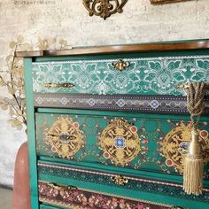 an old dresser painted green and gold with ornate designs on the top, along with other decorative items