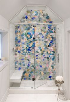 a bathroom with a glass shower door and colorful tiles on the wall, along with a bench