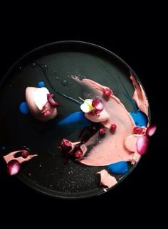 a black plate topped with pink and blue dessert next to another plate filled with fruit