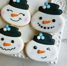 four decorated snowman cookies sitting on top of a white plate