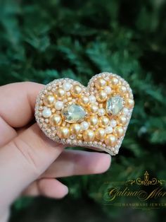 a person holding a heart shaped brooch with pearls and stones in it's center