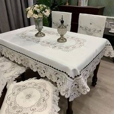 a dining room table with white linens and lace on the edges, along with matching chairs