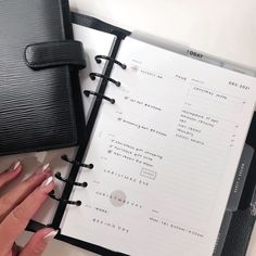 a woman's hand on top of an open planner next to a black purse